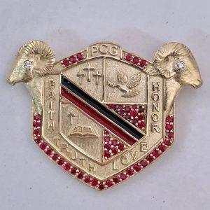 Lapel pin with seal with black enamel and red gemstones, and rams heads on the corners.
